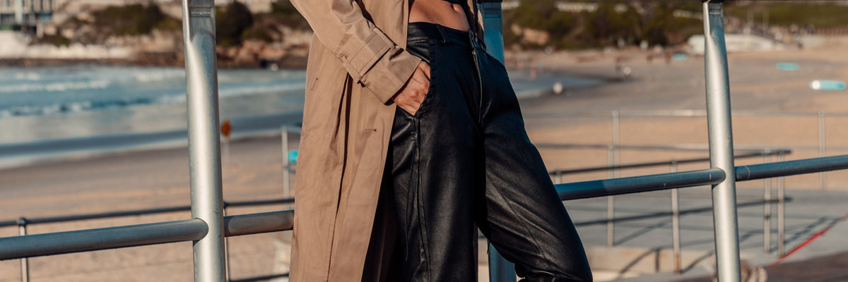 Women's leather pants by WEST 14TH: black leather pants worn with a trench coat on a beachside promenade